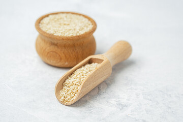 Natural sesame seeds in wooden scoop and jar on light countertop