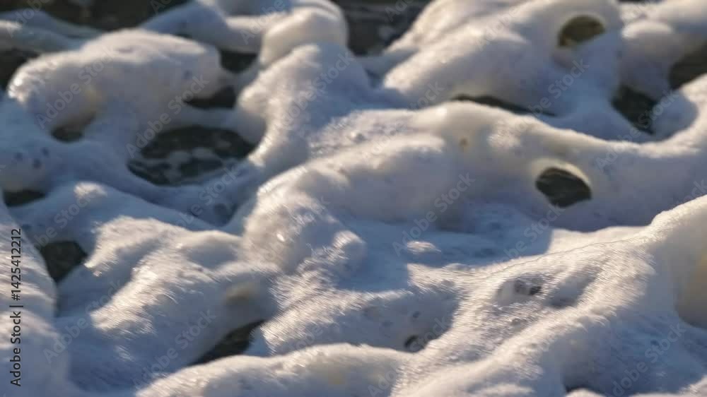Poster close-up video of frothy sea foam on a beach. captured at a low angle, showcasing the intricate patt