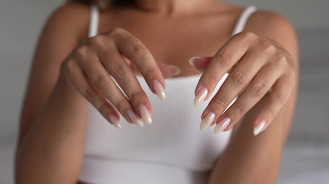 Close-up of a young woman showcasing her almond-shaped nails with pearly pink gel polish. A soft and elegant beauty moment highlighting manicure, self-care and feminine style