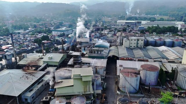 High aerial shot captures smokestacks of coastal factories belching smoke over squatted shanty homes along the Cagayan de Oro shoreline, revealing environmental and social contrasts.