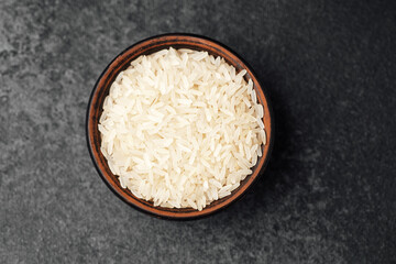 Bowl of uncooked white rice on a dark stone background