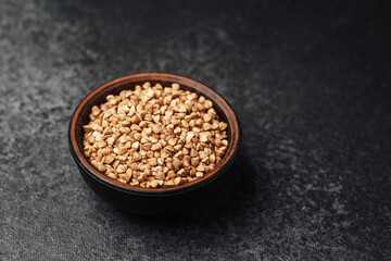 Buckwheat seeds in a bowl on a dark surface with natural lighting