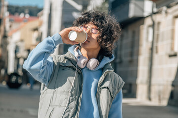 young man with headphones and phone drinking coffee on the street