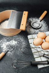 Kitchen tools for baking with flour, eggs, and whisks on black background