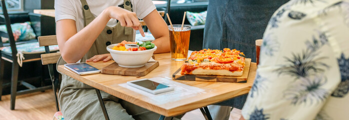 Banner of unrecognizable young girl pointing with her finger to healthy poke bowl while enjoy lunch with friend sitting at the restaurant table, in a lively atmosphere of togetherness and conversation