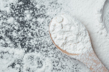 White flour on a wooden spoon scattered on a dark surface in a kitchen