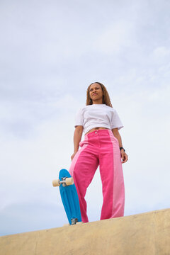 Stylish woman holding skateboard and looking away in skate park