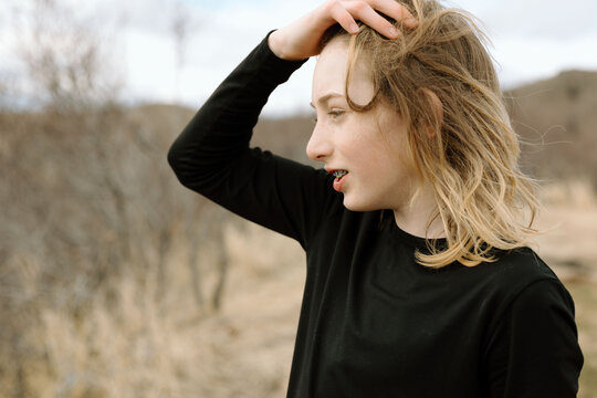 Teen boy runs hand through hair on breezy hill