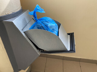 Blue disposable plastic bag of trash in the manhole door of the garbage chute indoor entrance of an...