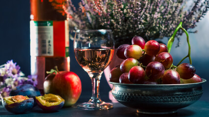 ripe grapes with a glass of wine with an apple with plums and flowers