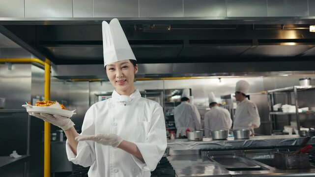 Women chef in uniform holding a perfectly plated dish, with the main ingredient prominently displayed in the center. A perfect footage for restaurant menus or food blogs, showing a delicious plate