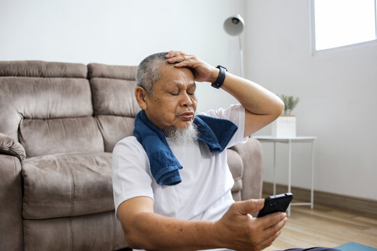 Elderly Asian man in sportswear using smartphone frowning upset due to having problem.