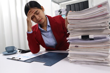 A woman in a red blazer sits at a desk with appearing stressed or exhausted. The background shows office shelves filled with binders and more files, emphasizing a busy and overwhelming work environmen