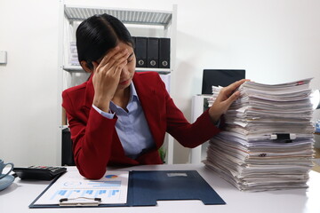 A woman in a red blazer sits at a desk with appearing stressed or exhausted. The background shows office shelves filled with binders and more files, emphasizing a busy and overwhelming work environmen