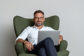 Man sitting on a green armchair with a laptop computer, isolated against a white background.