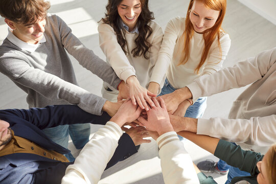 Group of people stacking hands, involved in teambuilding activity, gesturing after goal achievement, demonstrate nice team work, posing in circle. Cooperation, support and unity concept