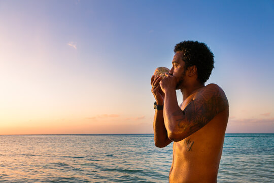 Fijian man blowing traditional conch shell at sunset, Fiji
