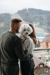 Couple embracing on balcony with their dog, enjoying mountain view