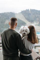 Couple embracing and holding their dog while admiring mountain view from hotel balcony