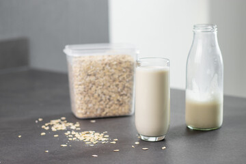A glass of oat milk and oatmeal in a box on grey kitchen table. Vegan and non-dairy alternative milk