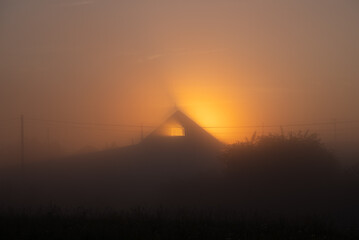Golden sunlight streaming through a foggy rural landscape, illuminating a serene barn and creating a mystical, atmospheric scene filled with tranquility and beauty © wifesun