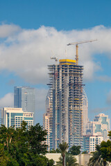 Fototapeta premium Modern Building Under Construction with Red Crane. High-rise building construction site with red tower crane lifting materials