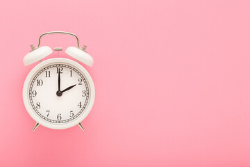 White alarm clock on light pink table background. Pastel color. Closeup. Time concept. Empty place for text. Top down view.