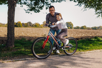 Fototapeta premium Father teaching daughter riding bicycle in countryside