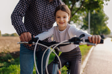 Obraz premium Father helping daughter learning to ride bicycle on a sunny day
