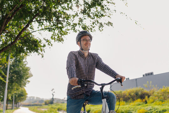 Man riding bicycle in park wearing helmet and smiling