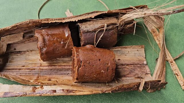 Palm sugar wrapped in dried banana leaves has been opened and the sugar can be seen isolated on a green background.
