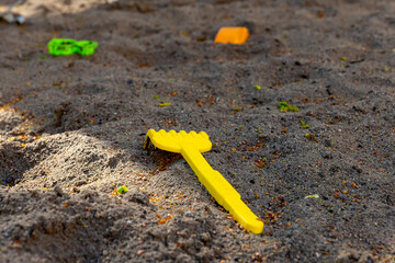 Bright yellow toy rake lies in sandy playground as children play nearby in the warm afternoon light