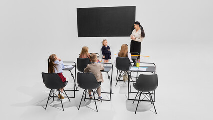 Cheerful girl presenting in front of classmates with teacher watching, full of confidence. Concept of education, school speech, individual achievement, classroom dynamics, learning development.