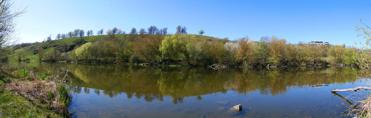 Modern private house over the river. The modern house stands on a hill above the river. The calm flow of the river surrounded by spring nature.