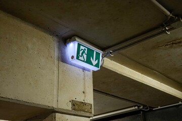 Illuminated green emergency exit sign showing escape route in underground parking garage