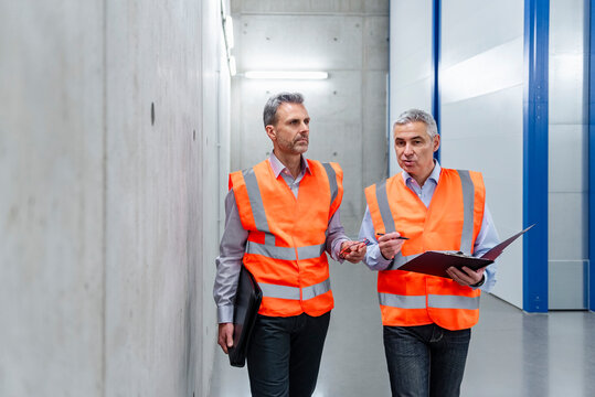 Two professionals in safety vests discussing in a storage hall