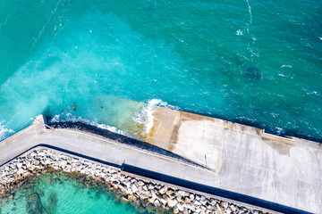 Aerial drone image of a seawall with coastal. Beacon at the tip of a rocky breakwater.