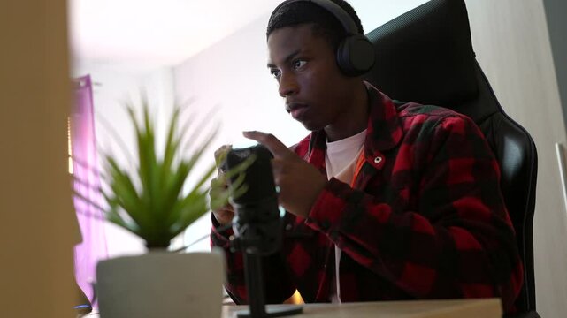 African american young man playing video games, broadcasting live gameplay through online streaming platform, wearing gaming headset, sitting in home studio setup
