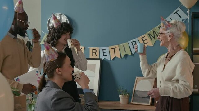 Medium shot of elderly Caucasian woman in party attire toasting with younger colleagues during her retirement celebration, surrounded by decorations, balloons, and warm smiles in office