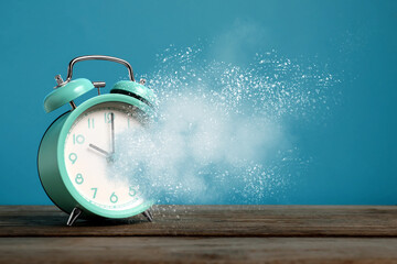 Alarm clock dissolving on wooden table against light blue background. Time is running out