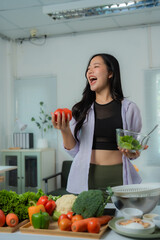 Beautiful young asian woman is laughing while preparing a healthy vegan meal with fresh vegetables...