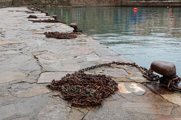 Several rusty chains and secure mooring points are visible on a stone pier, reflecting a serene...