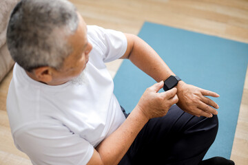 Above view of senior man looking at smartwatch or tracker while exercising at home