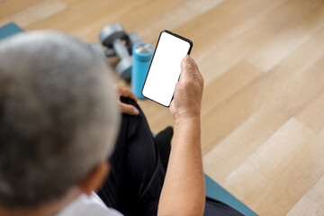 Old man sit on mat holding phone with mock up screen for fitness app at home