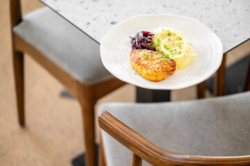 A plated meal featuring golden chicken breast with creamy mashed potatoes and red cabbage slaw, elegantly presented on a stylish table, perfect for a comforting dining experience.
