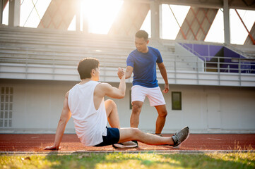 Asian man is pulling or grabbing his friend hand helping him to stand up after falling on racetrack.