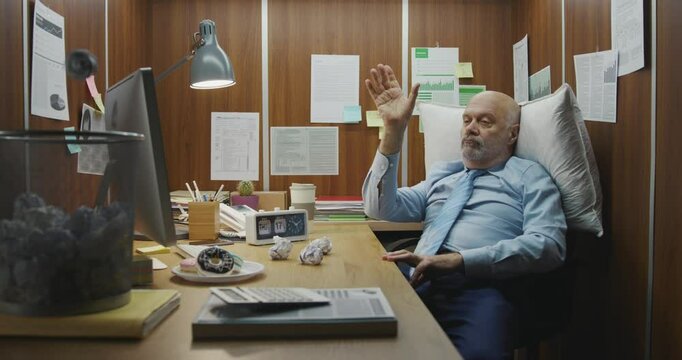 Bored lazy office worker sitting at his desk, he is throwing crumpled paper in the trash bin and wasting time instead of working