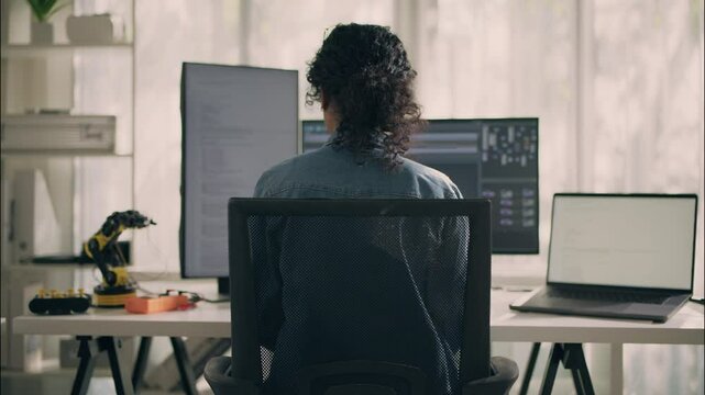 Close-up of Asian woman engineer in denim shirt concentrating while looking at monitor, holding pen. Office technology and developer workspace concept.