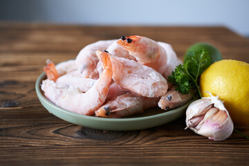 Frozen prawns on a plate with lemon and parsley on a wooden table