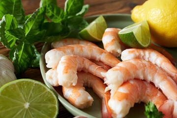 Shrimps with lime and herbs on wooden table, closeup